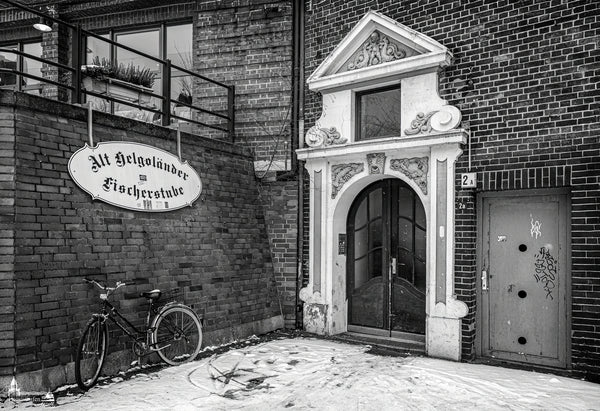 Verschneite Szene am Hamburger Fischmarkt mit der alten Helgoländer Fischerstube, verziertem Hauseingang und nostalgischem Fahrrad.