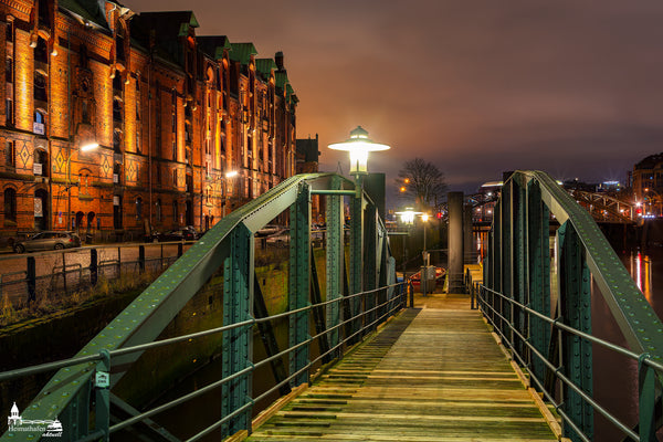 Abendliche Stimmung in der Hamburger Speicherstadt mit Anlegerbrücke und beleuchteten Backsteinfassaden.