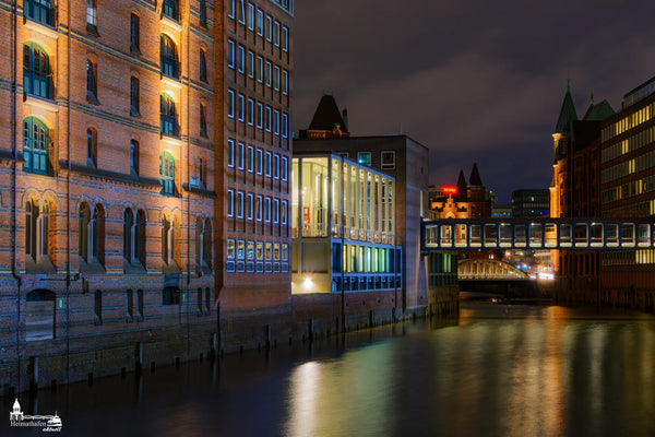 Die historische Hamburger Speicherstadt im nächtlichen Glanz – mit Lichterspiel an Backsteinfassaden und gläserner Brückenverbindung über dem Fleet.