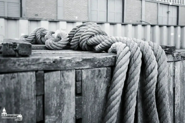 Stark gedrehtes Tauwerk auf rustikaler Holzkiste im Hafenbereich, Schwarz-Weiß-Aufnahme